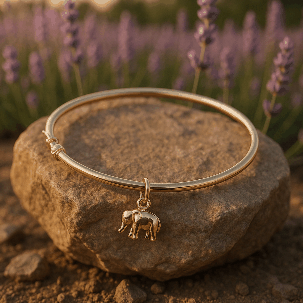 18K yellow gold elegant elephant bracelet with high-polish finish and secure clasp displayed on a rock with a blurred lavender background.