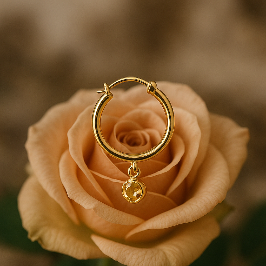 Bold 18K yellow gold Peruvian-style hoop earring with a dangling charm on a peach rose background