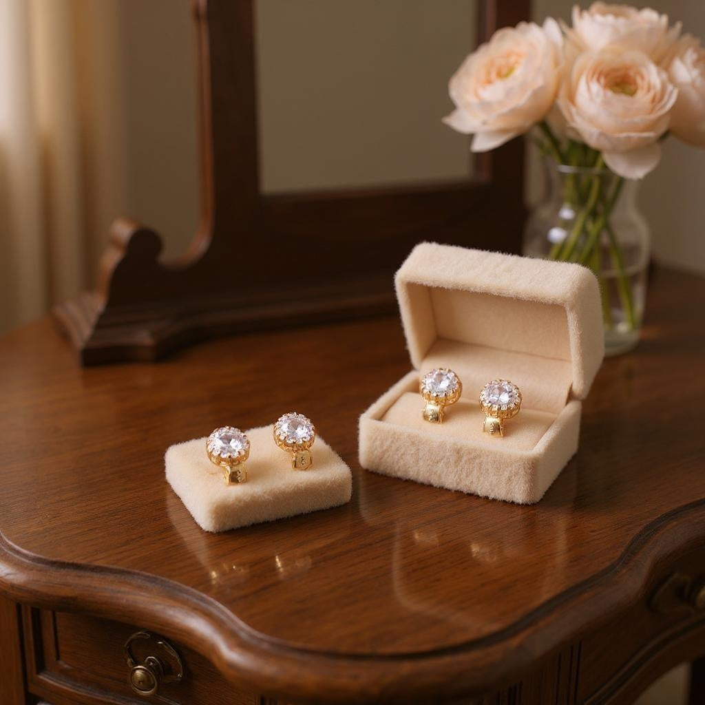 Elegant 18K yellow gold earrings with sparkling white stones displayed on a wooden table with a velvet jewelry box and soft floral background.