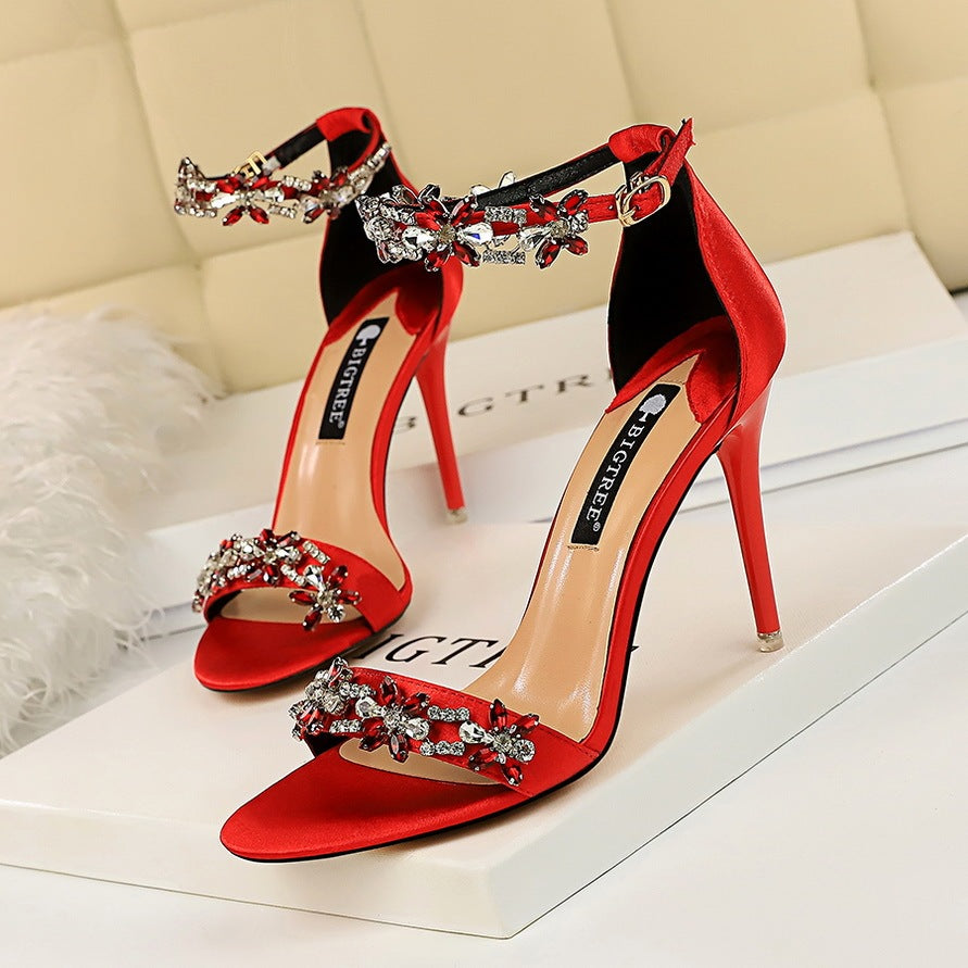Red high-heeled sandals with crystal embellishments on a white surface.